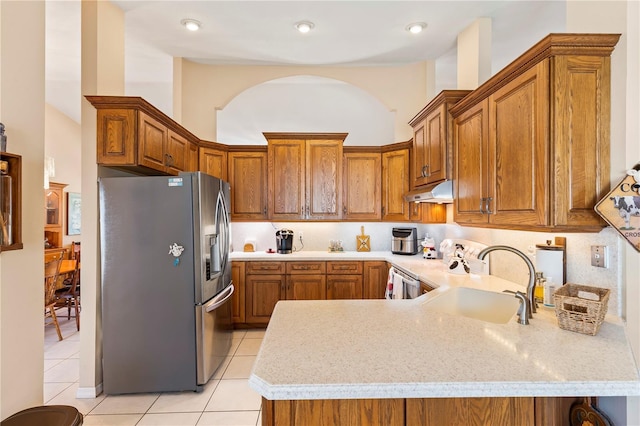 kitchen featuring a sink, under cabinet range hood, a peninsula, brown cabinetry, and stainless steel fridge with ice dispenser