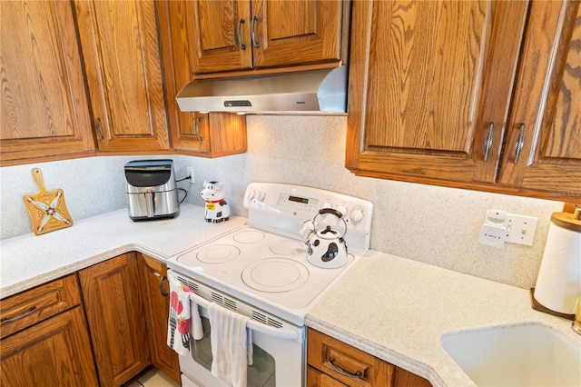 kitchen featuring under cabinet range hood, brown cabinetry, light countertops, and white electric range oven