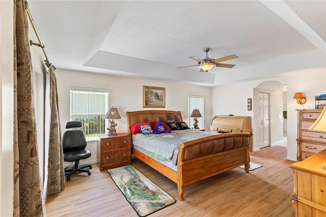 bedroom featuring baseboards, a raised ceiling, light wood-style floors, and arched walkways