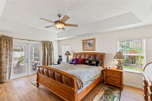 bedroom featuring light wood-style flooring, multiple windows, a tray ceiling, and access to outside