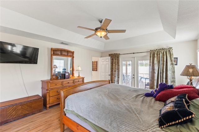 bedroom featuring visible vents, a tray ceiling, light wood-style flooring, french doors, and access to outside