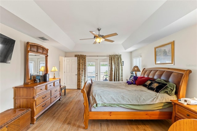 bedroom with access to exterior, visible vents, light wood finished floors, ceiling fan, and a tray ceiling