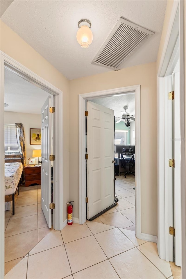 corridor featuring light tile patterned flooring, baseboards, visible vents, and a textured ceiling