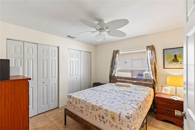 bedroom with light tile patterned floors, visible vents, two closets, and a ceiling fan