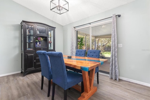 dining area featuring a chandelier, baseboards, lofted ceiling, and wood finished floors