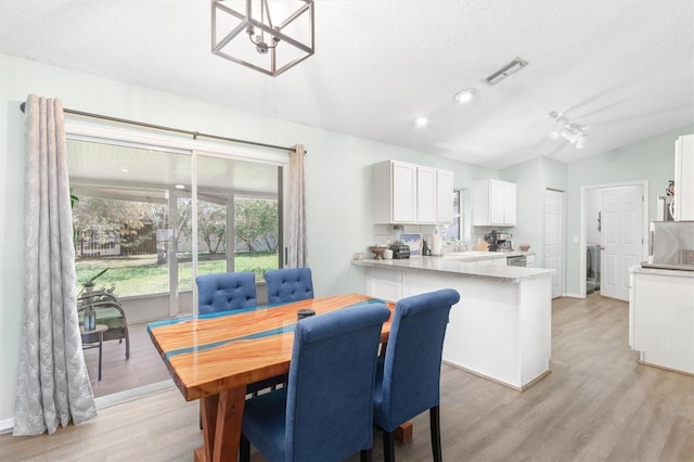 dining space with visible vents, a textured ceiling, light wood-style floors, and vaulted ceiling