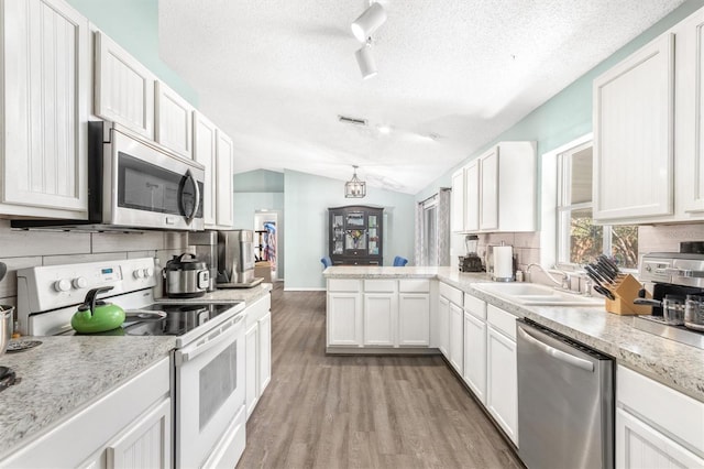 kitchen with lofted ceiling, decorative backsplash, light wood-style floors, stainless steel appliances, and a sink