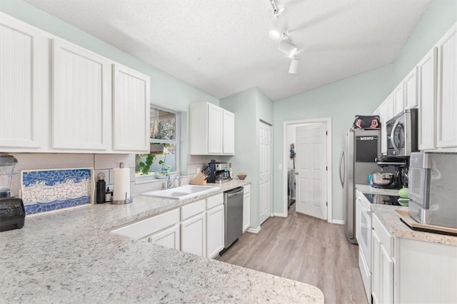 kitchen with white cabinetry, stainless steel appliances, lofted ceiling, and a sink