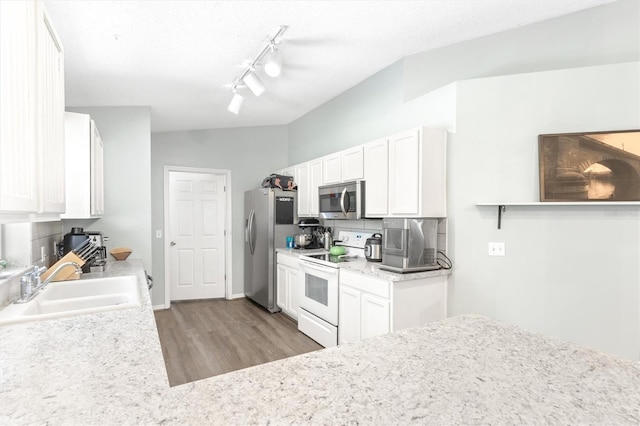 kitchen with wood finished floors, a sink, appliances with stainless steel finishes, white cabinetry, and backsplash