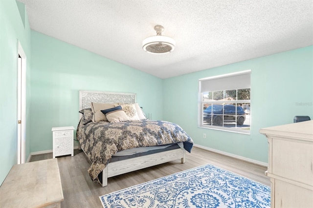 bedroom with lofted ceiling, wood finished floors, baseboards, and a textured ceiling