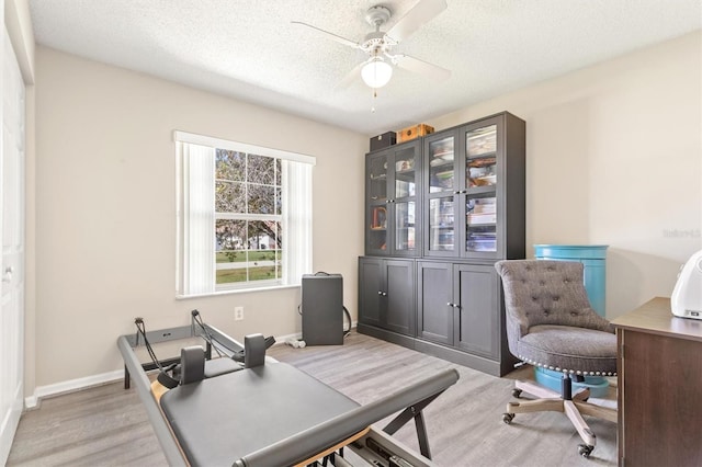 office space with ceiling fan, baseboards, light wood-type flooring, and a textured ceiling