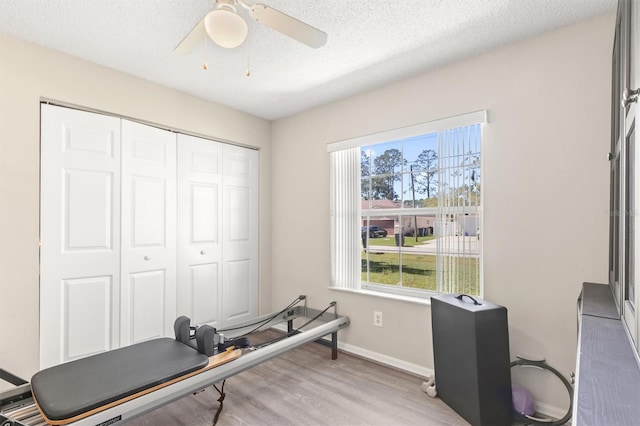 workout area featuring ceiling fan, baseboards, a textured ceiling, and light wood-style flooring