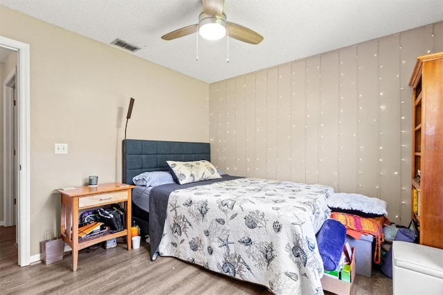 bedroom with visible vents, a ceiling fan, a textured ceiling, wood finished floors, and baseboards