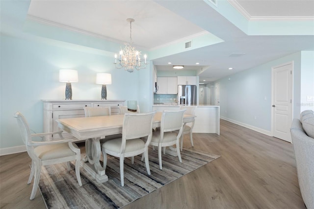 dining area featuring a tray ceiling, baseboards, ornamental molding, and light wood finished floors