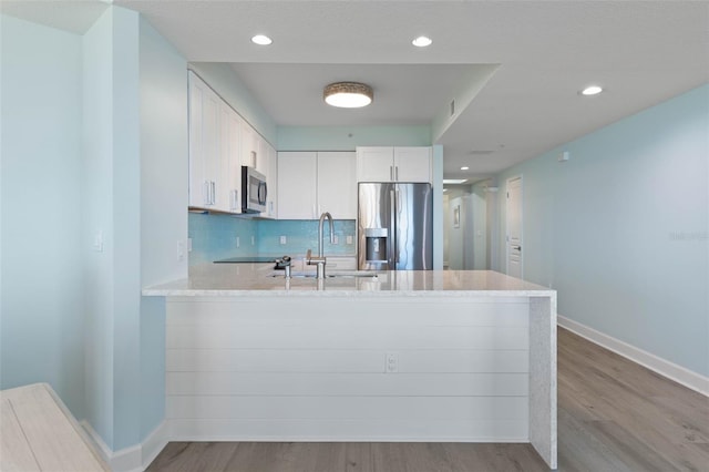 kitchen with a peninsula, a sink, stainless steel appliances, white cabinets, and backsplash