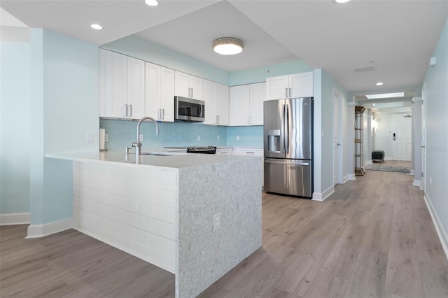 kitchen featuring a peninsula, a sink, light countertops, appliances with stainless steel finishes, and light wood-type flooring