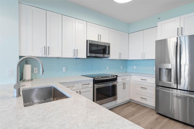 kitchen with a sink, light wood-type flooring, appliances with stainless steel finishes, and white cabinetry