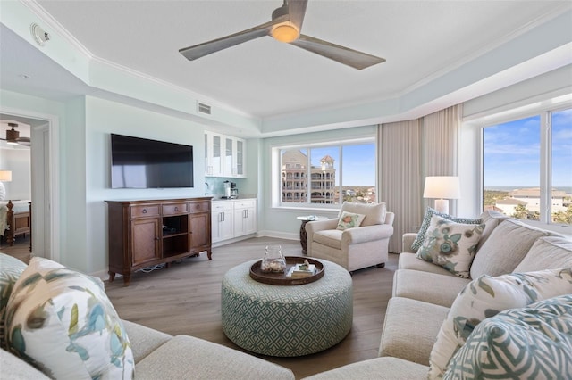 living room featuring baseboards, visible vents, light wood-style flooring, ornamental molding, and ceiling fan