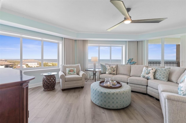 living area featuring a wealth of natural light, light wood-type flooring, baseboards, and a ceiling fan