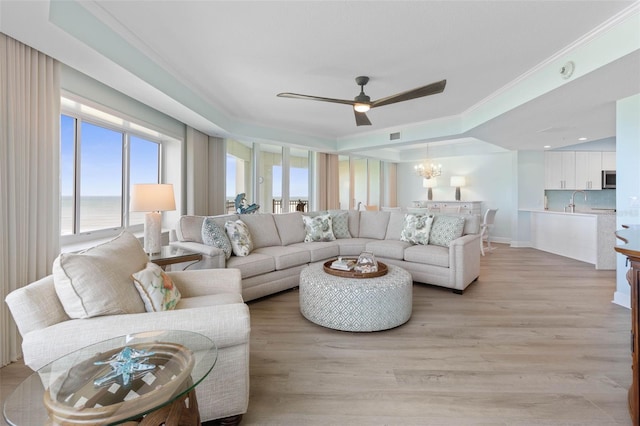 living room with a wealth of natural light, ceiling fan with notable chandelier, light wood finished floors, and crown molding