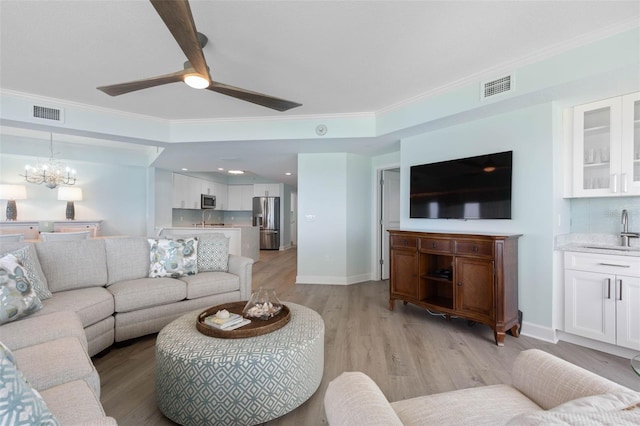 living area featuring visible vents, baseboards, crown molding, and light wood-style floors