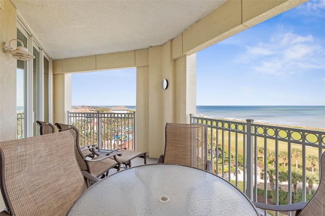 balcony with outdoor dining space, a view of the beach, and a water view