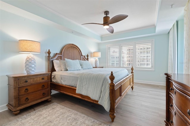 bedroom with a ceiling fan, baseboards, a tray ceiling, crown molding, and light wood-type flooring