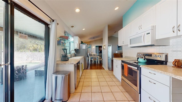 kitchen with light tile patterned floors, a sink, white cabinets, appliances with stainless steel finishes, and backsplash