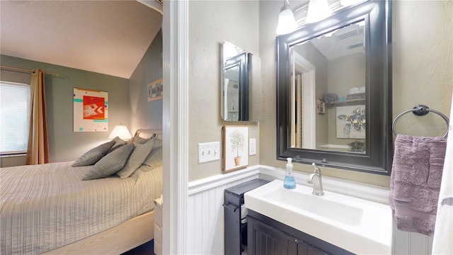 bathroom with a wainscoted wall, vanity, and vaulted ceiling