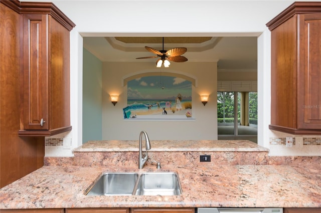 kitchen with a tray ceiling, ornamental molding, brown cabinets, and a sink