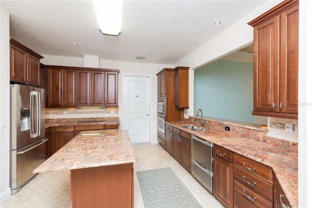 kitchen featuring light stone countertops, a sink, appliances with stainless steel finishes, backsplash, and a center island