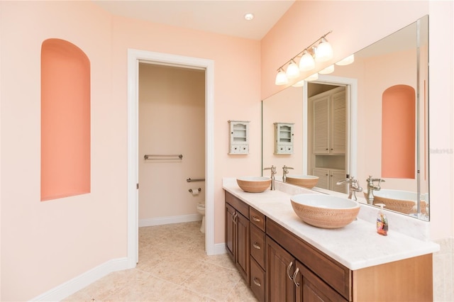 full bathroom featuring double vanity, toilet, baseboards, and a sink