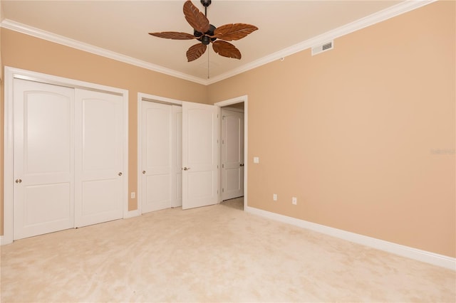 unfurnished bedroom with visible vents, multiple closets, light colored carpet, and crown molding