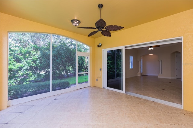 unfurnished sunroom featuring arched walkways and ceiling fan