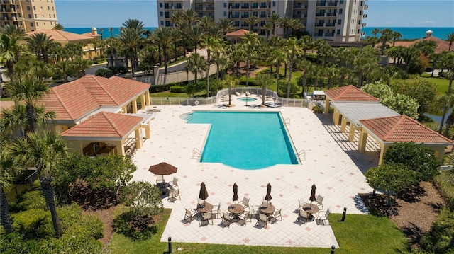 pool with a community hot tub, a water view, a patio, and fence