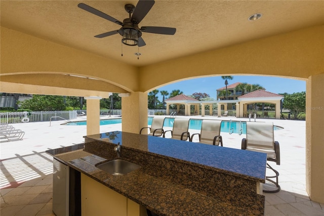 view of patio with outdoor dry bar, fence, a gazebo, a community pool, and a sink