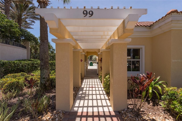 view of exterior entry with stucco siding, a tile roof, and a gate