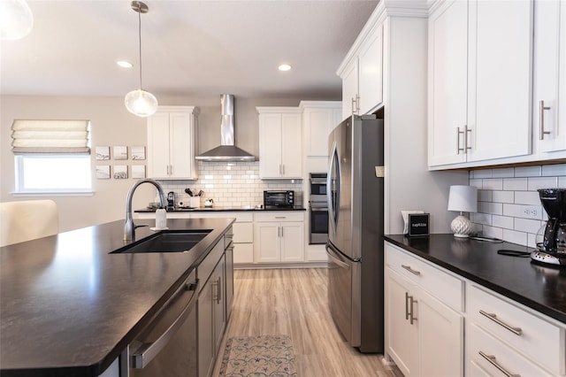 kitchen featuring a sink, stainless steel appliances, white cabinetry, dark countertops, and wall chimney range hood