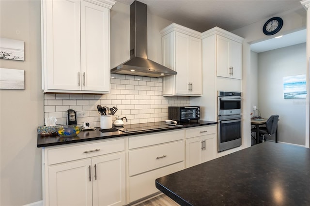 kitchen featuring white cabinetry, dark countertops, wall chimney exhaust hood, and tasteful backsplash