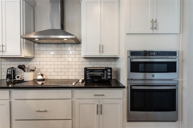 kitchen featuring black electric cooktop, double oven, dark countertops, and wall chimney range hood