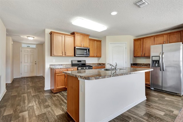 kitchen featuring visible vents, a kitchen island with sink, a sink, appliances with stainless steel finishes, and dark wood-style flooring