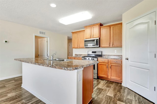 kitchen with dark wood-style floors, visible vents, an island with sink, a sink, and appliances with stainless steel finishes