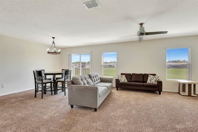 living area featuring visible vents, light carpet, baseboards, and ceiling fan with notable chandelier