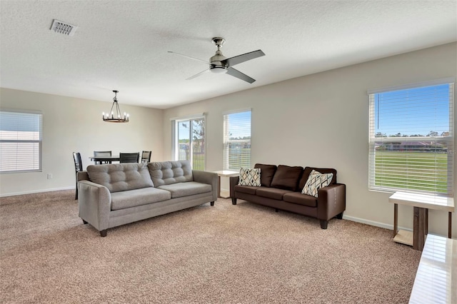 living area with a textured ceiling, ceiling fan with notable chandelier, visible vents, and light carpet