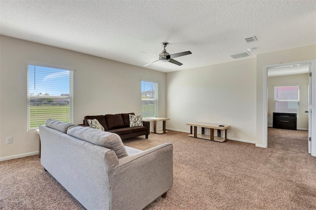 living area with visible vents, a ceiling fan, a textured ceiling, baseboards, and light colored carpet