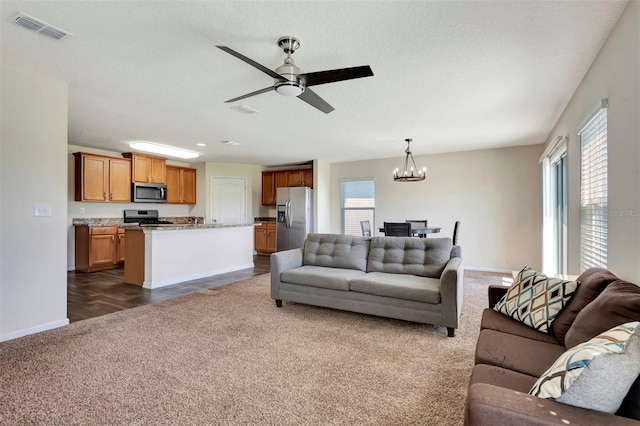 living area featuring dark colored carpet, visible vents, a healthy amount of sunlight, and ceiling fan with notable chandelier