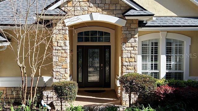 entrance to property featuring stone siding and roof with shingles