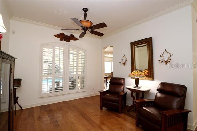 sitting room with ornamental molding, a ceiling fan, wood finished floors, arched walkways, and baseboards