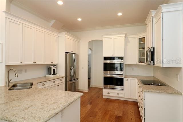 kitchen featuring ornamental molding, appliances with stainless steel finishes, a peninsula, arched walkways, and a sink