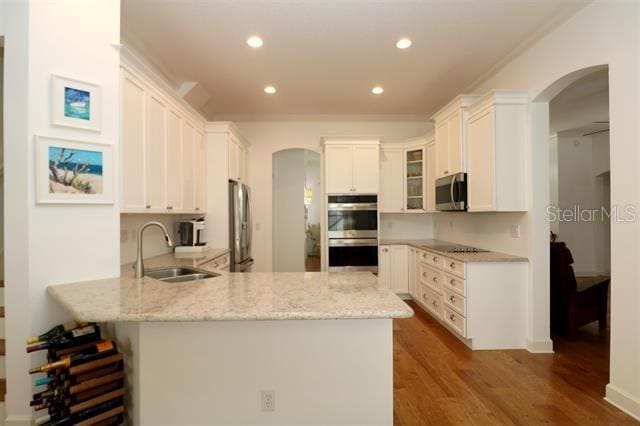 kitchen featuring glass insert cabinets, a peninsula, arched walkways, stainless steel appliances, and a sink